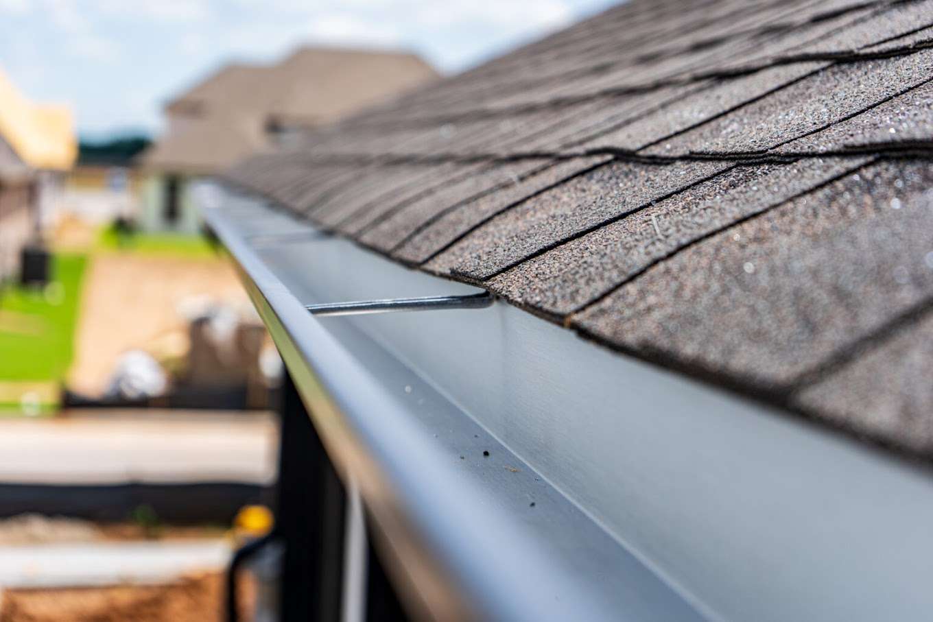 Close-up of asphalt shingles on a roof edge with a metal gutter, showcasing quality roofing construction and materials relevant to Artisan Roofing Construction services.