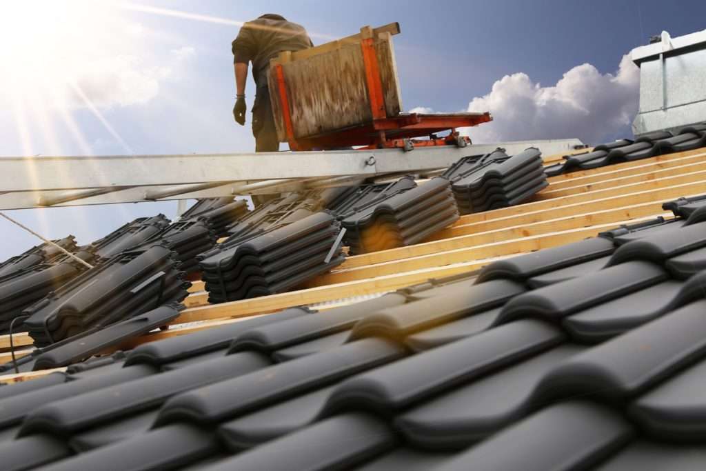Roofer installing black tile roofing on a residential structure, emphasizing durable and energy-efficient roofing solutions.