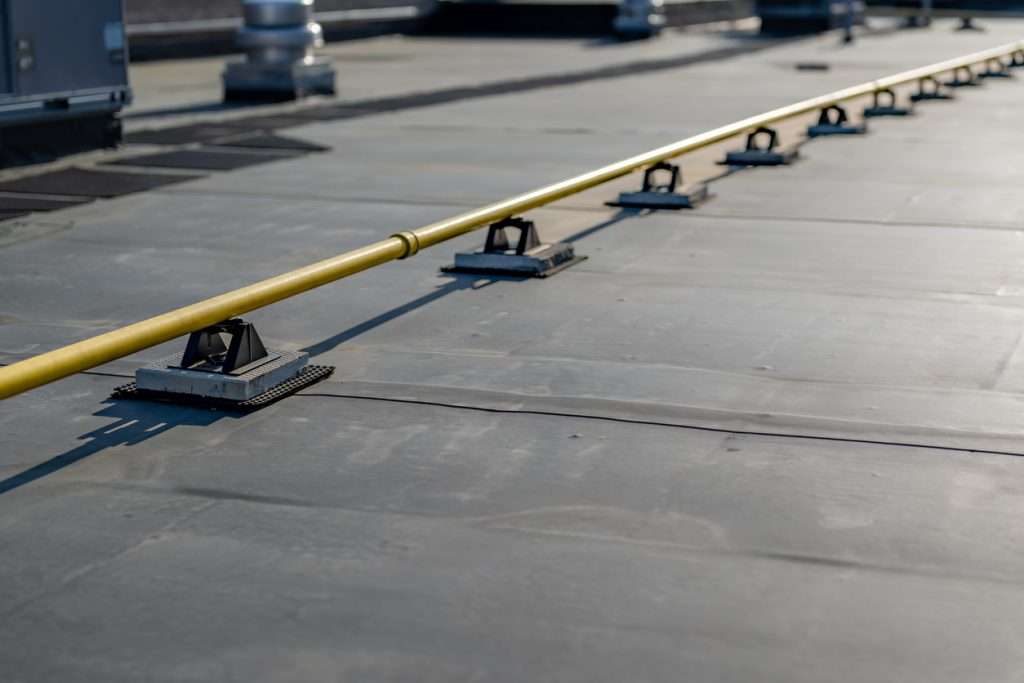 Roofing safety rail system on a commercial flat roof, showcasing yellow safety rail and supporting bases on a durable roofing membrane.