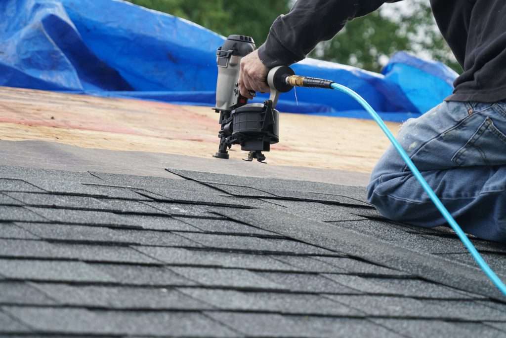 Person using a nail gun to install asphalt shingles on a roof, showcasing quality roofing craftsmanship for residential and commercial projects.
