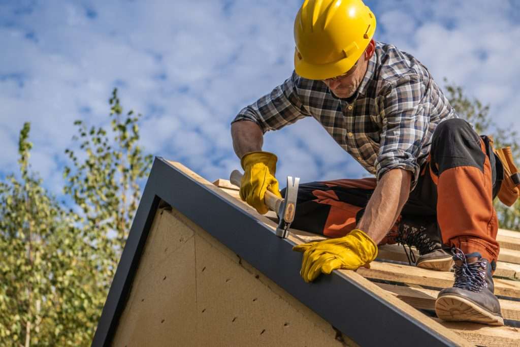 Man installing roofing materials on a house, wearing a hard hat and gloves, demonstrating roofing construction techniques for budget-friendly options.