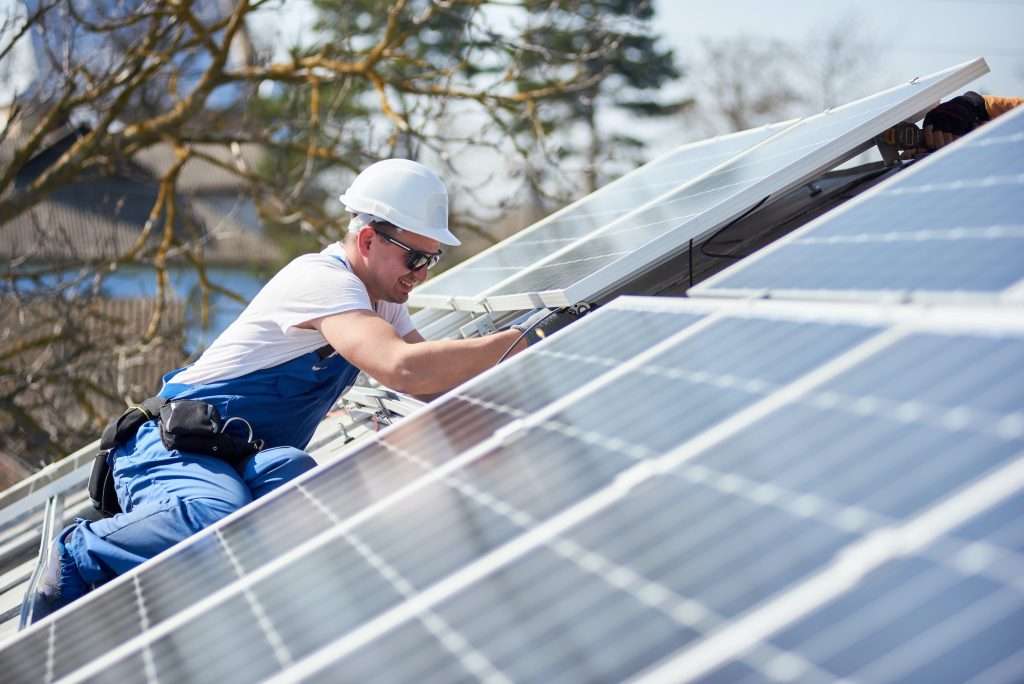 Worker installing solar photovoltaic panels on a commercial roof, showcasing energy-efficient roofing solutions by Artisan Roofing & Construction.