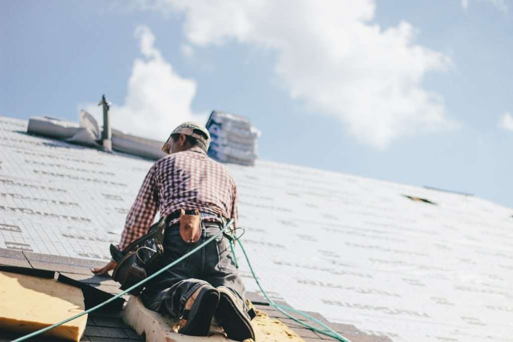 Roofer installing shingles on a commercial roof, showcasing professional craftsmanship and high-performance materials under a clear blue sky.