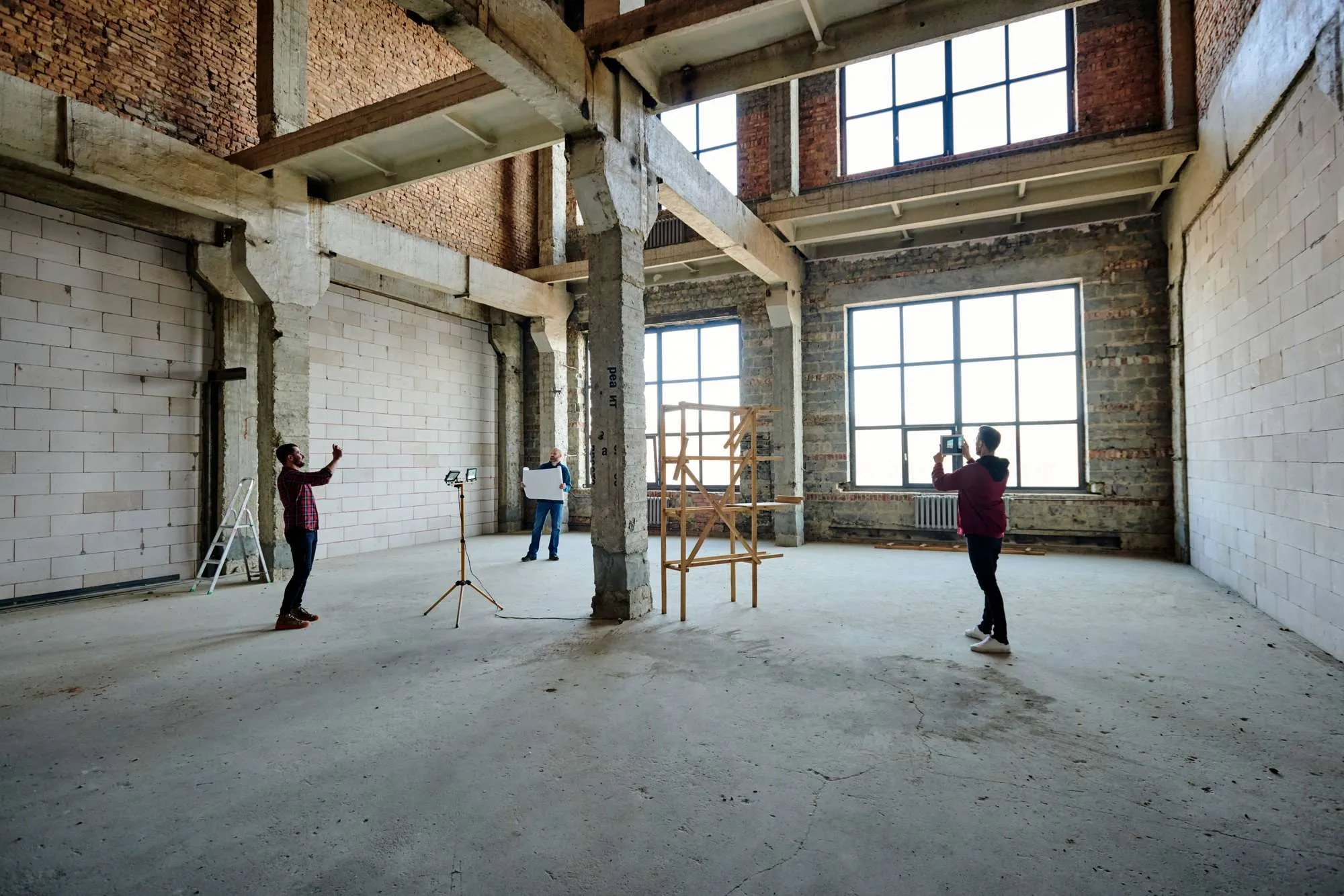 Two young contractors photographing an unfinished construction site with large windows, showcasing a commitment to innovation and quality in the building process.