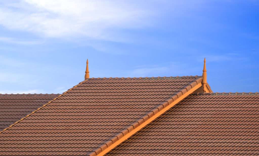 Brown ceramic tile roof with vintage style peaks against a clear blue sky, illustrating aesthetic roofing options for enhancing home value and curb appeal.