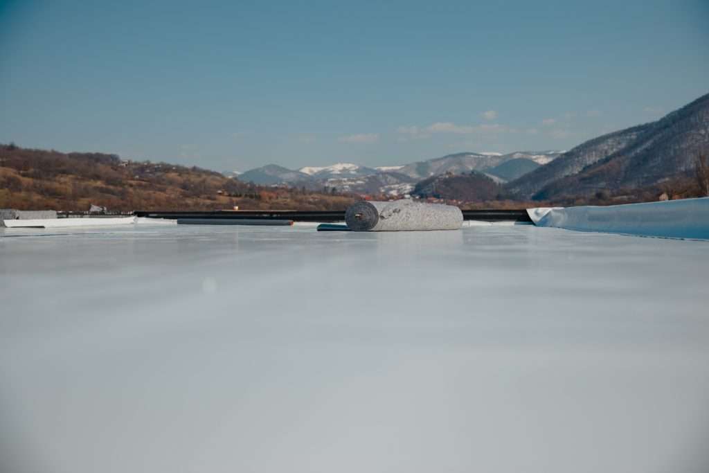 Flat commercial roofing with a rolled material on the surface, overlooking a mountainous landscape, illustrating roofing installation and maintenance techniques.