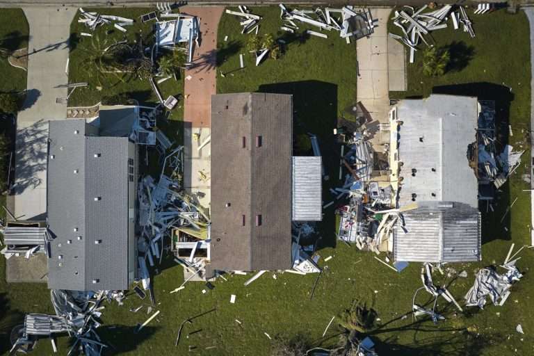 Aerial view of residential homes with storm damage, including debris scattered across yards and roofs, illustrating the impact of severe weather on properties.