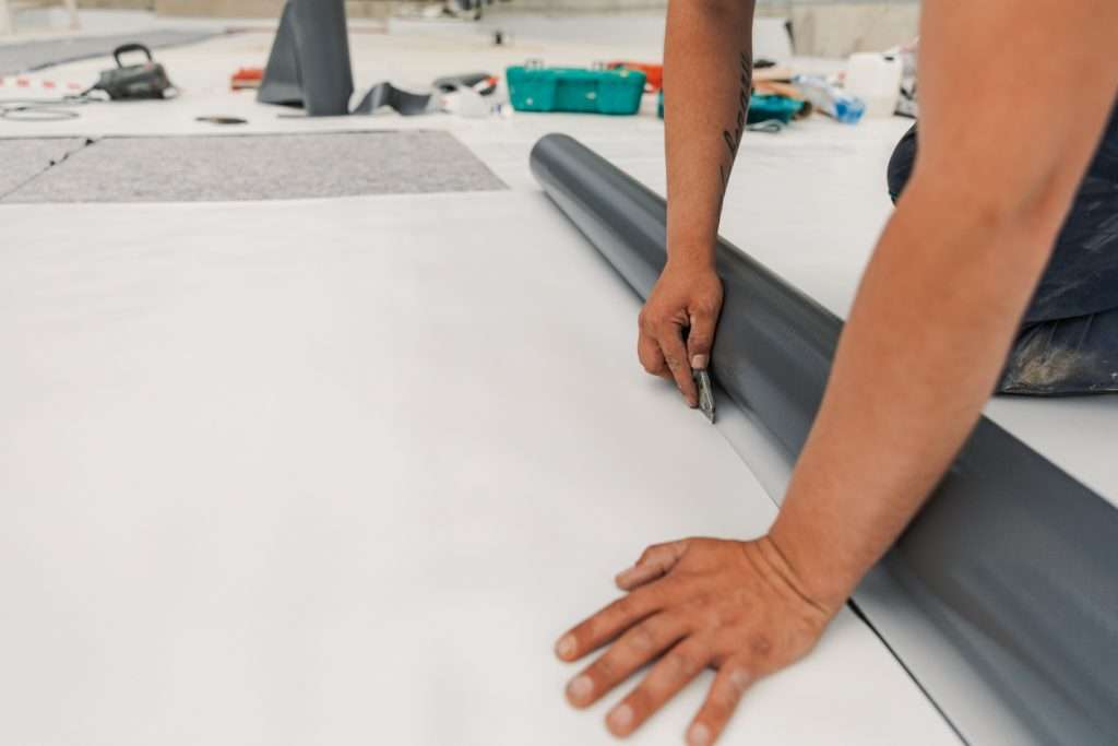Worker cutting roofing material for commercial roof installation, emphasizing maintenance and energy efficiency benefits.