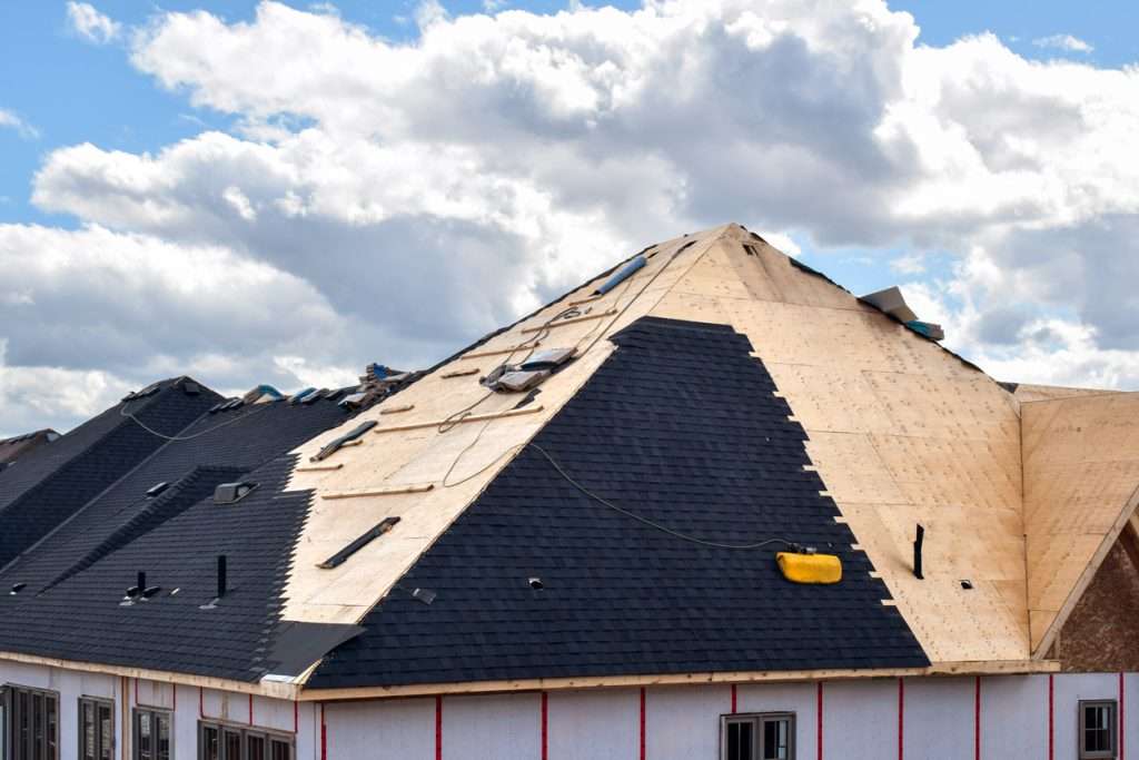 Roof under construction featuring dark shingles and exposed plywood, illustrating the roofing services offered by Artisan Roofing & Construction, emphasizing roof inspection and maintenance.