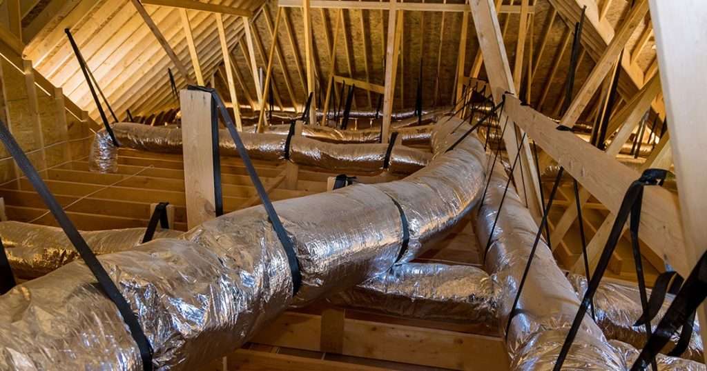 Attic interior with insulated ductwork and wooden framing, illustrating proper ventilation and insulation crucial for energy efficiency with black shingles.