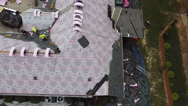 Roof replacement in progress on a residential home, featuring workers applying underlayment and shingles, with surrounding materials and equipment visible, illustrating the complexities of roofing projects and the importance of proper techniques for structural integrity.