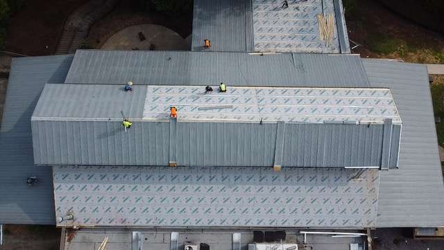 Roofing crew working on a commercial building installation, featuring metal roofing panels and protective underlayment, emphasizing professional roofing services by Artisan Roofing & Construction.
