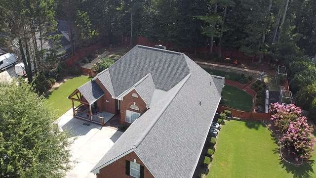 Aerial view of a well-maintained residential home with a new roof, surrounded by a lush green lawn and landscaped garden, showcasing Artisan Roofing & Construction's quality craftsmanship in roofing and exterior services.