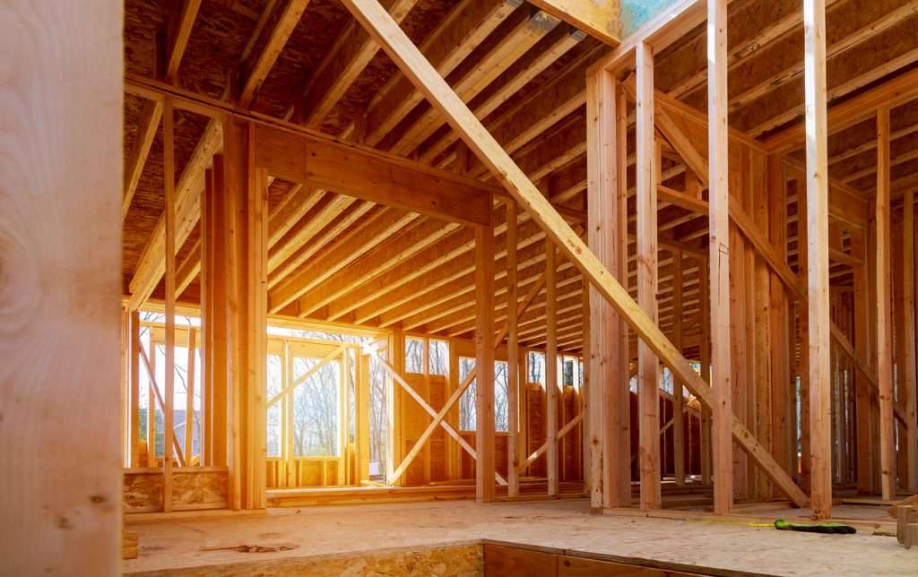 Interior view of a new home construction site, showcasing wooden framing and beams, emphasizing the building process by Artisan Roofing & Construction.