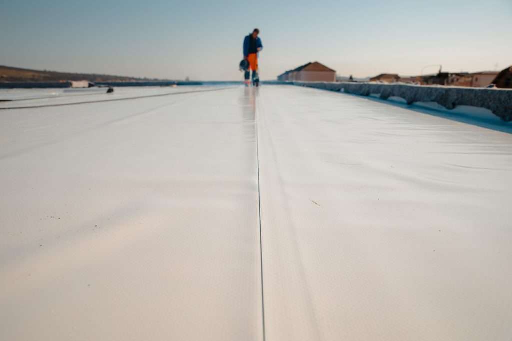 Commercial roofing installation in progress, featuring a worker on a flat white TPO roof, showcasing energy-efficient materials and craftsmanship by Artisan Roofing & Construction.