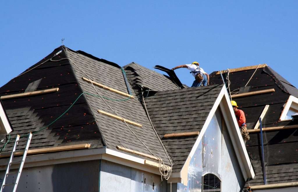 Roofers installing asphalt shingles on a residential roof, showcasing craftsmanship and construction techniques relevant to roofing services.