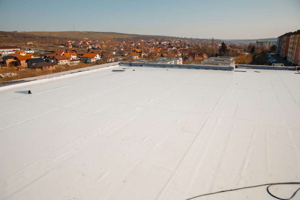 Flat commercial roof with white membrane, overlooking a residential area, emphasizing the importance of regular roof maintenance and cleaning for longevity and property aesthetics.