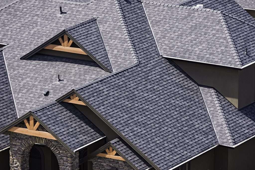 Aerial view of a residential roof featuring black shingles, showcasing intricate architectural details and overlapping shingle design, relevant to roofing materials and services provided by Artisan Roofing & Construction.