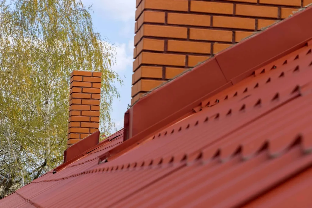 Red metal roof with brick chimneys and surrounding greenery, illustrating roof color choices that enhance home value and neighborhood aesthetics.