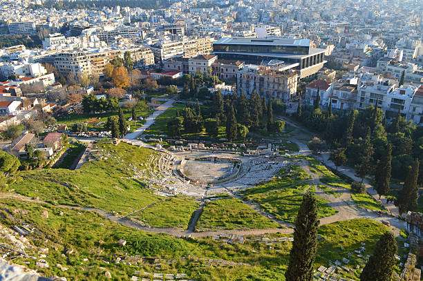 Aerial view of the ancient theater in Athens, surrounded by modern buildings and greenery, highlighting the blend of historic and contemporary architecture.