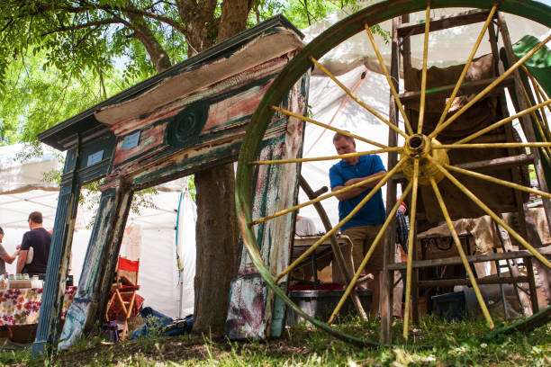 Artisan Roofing Construction display at a local event in Braselton, GA, featuring a vintage wagon wheel and colorful artistic installation, with a vendor interacting with attendees in a vibrant outdoor setting.
