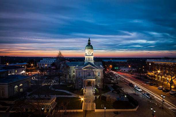 Buford, GA cityscape at dusk featuring historic courthouse with clock tower, illuminated streets, and vibrant sunset sky, reflecting the local charm and community spirit emphasized by Artisan Roofing & Construction's services.