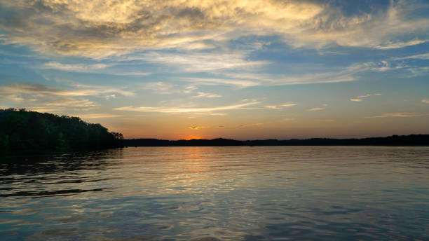 Scenic sunset over Lake Hartwell, reflecting vibrant colors on calm waters, surrounded by lush greenery and distant hills, representing the natural beauty of Hartwell, GA.