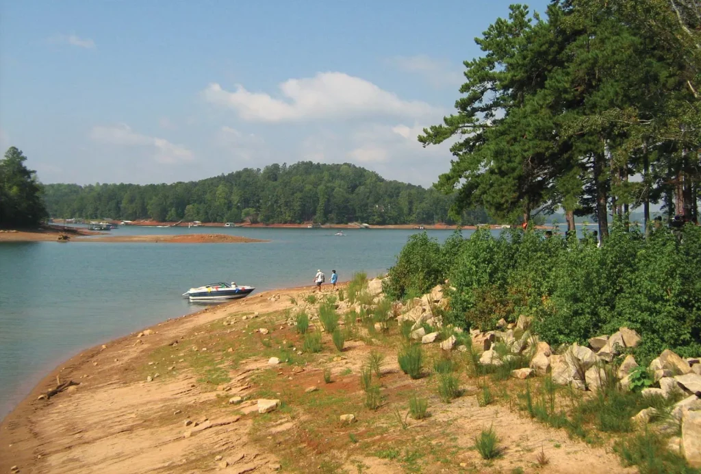 Gainesville, GA lakefront scene with a sandy shore, lush greenery, and a boat, capturing the vibrant outdoor lifestyle and recreational opportunities in the area.