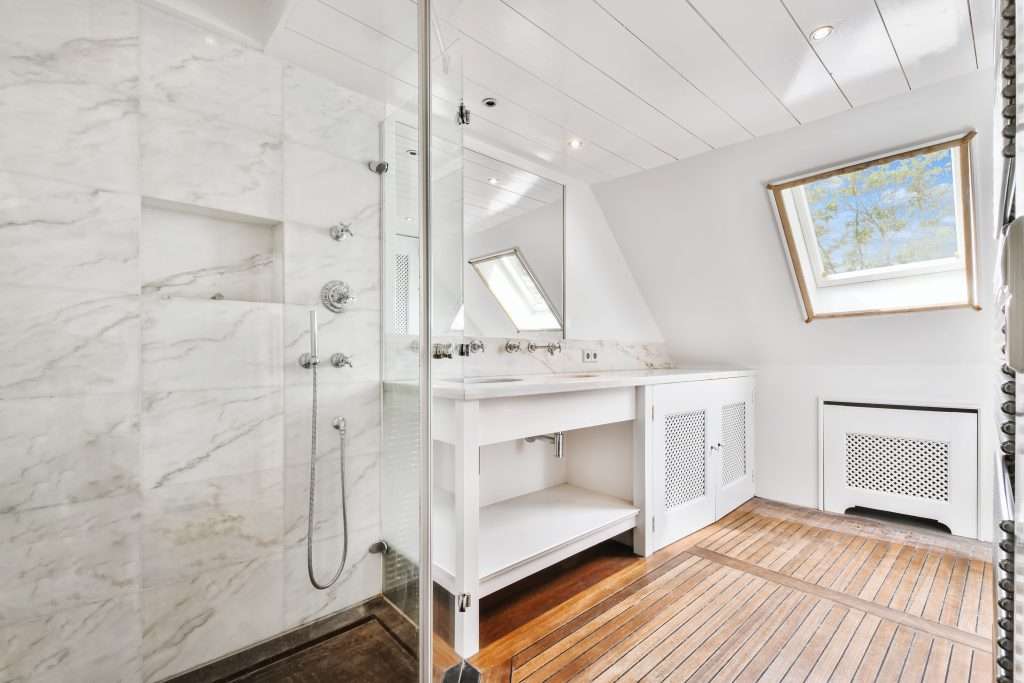 Modern bathroom interior featuring a marble shower, sleek sink with mirror, and wooden flooring, emphasizing stylish design for kitchen remodeling services by Artisan Roofing Construction.