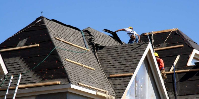 Construction workers putting shingles on the roof of a house.