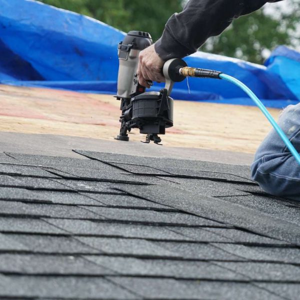 handyman using nail gun to install shingle to repair roof
