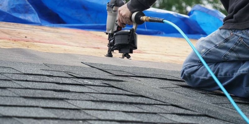 handyman using nail gun to install shingle to repair roof